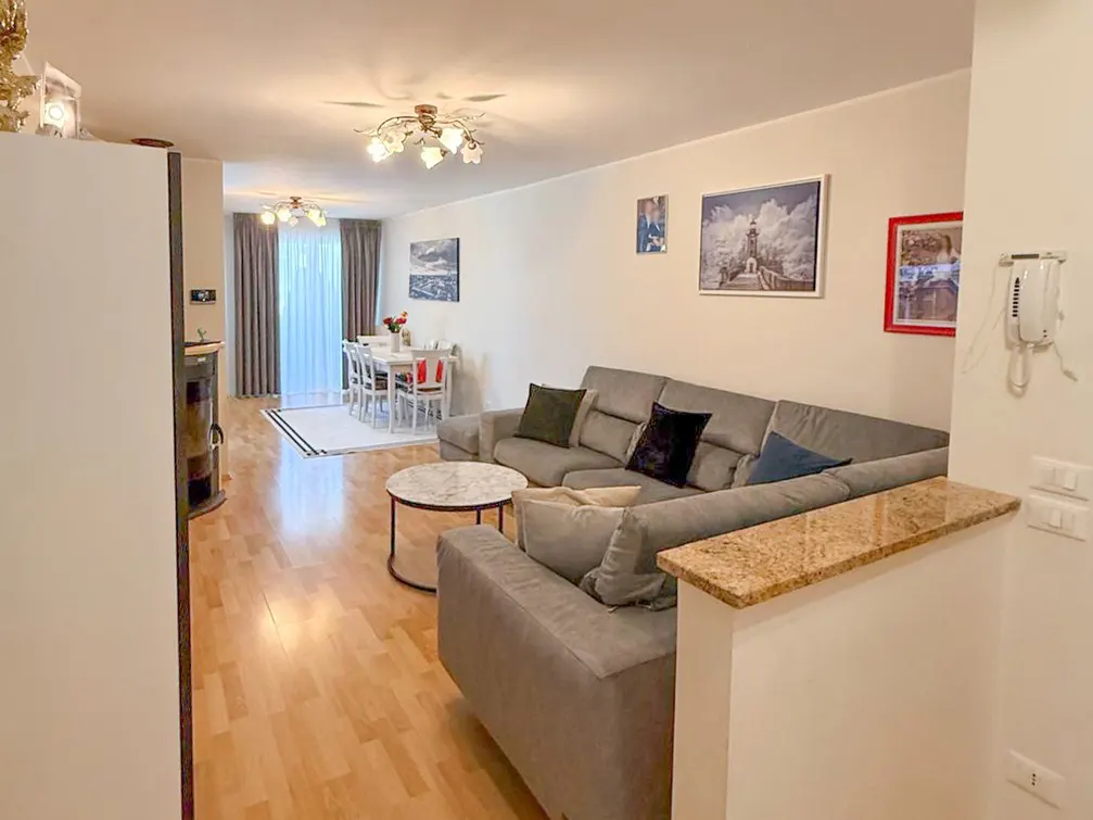 A bright living room with a gray sectional sofa, a round marble table, and a dining area with white chairs.