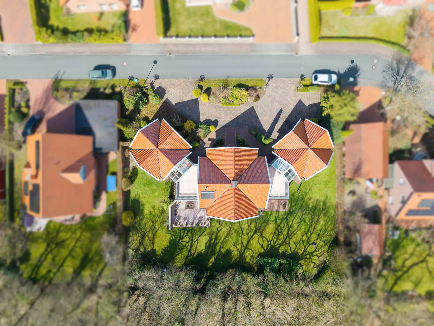 Aerial view of a house with orange roofs, green lawn, and a driveway with cars parked.