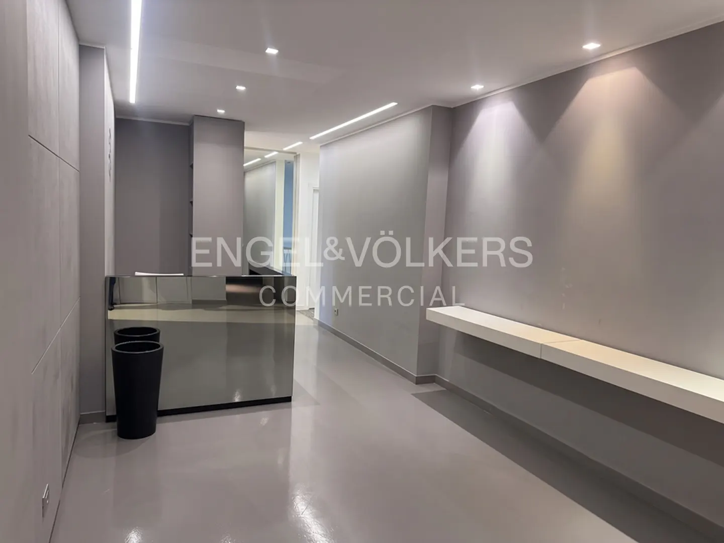 Modern office lobby with gray walls, a reflective reception desk, a floating shelf, and recessed ceiling lighting.