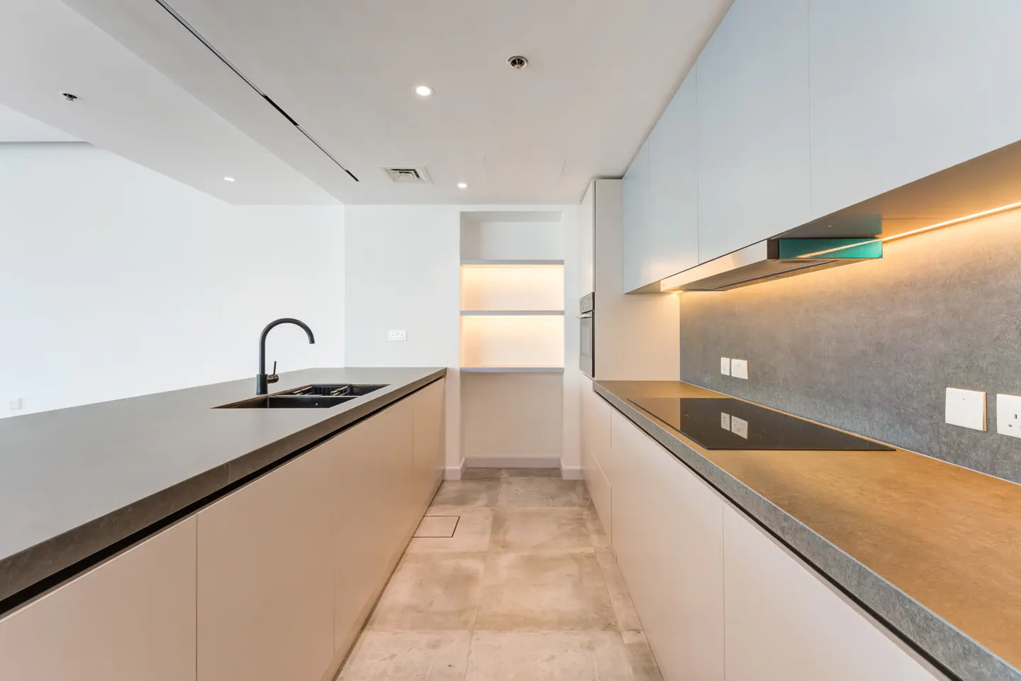 A modern kitchen with white cabinets, gray countertops, and a black faucet. There is a built-in oven and a cooktop.