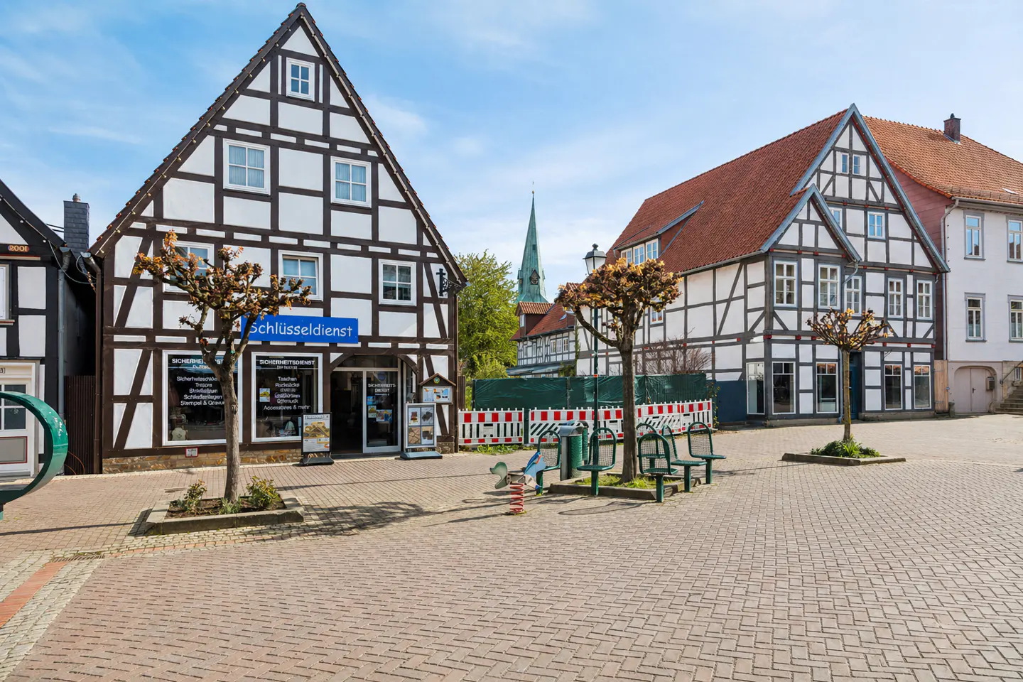 Town square with half-timbered buildings, benches, and a locksmith shop under a blue sky.
