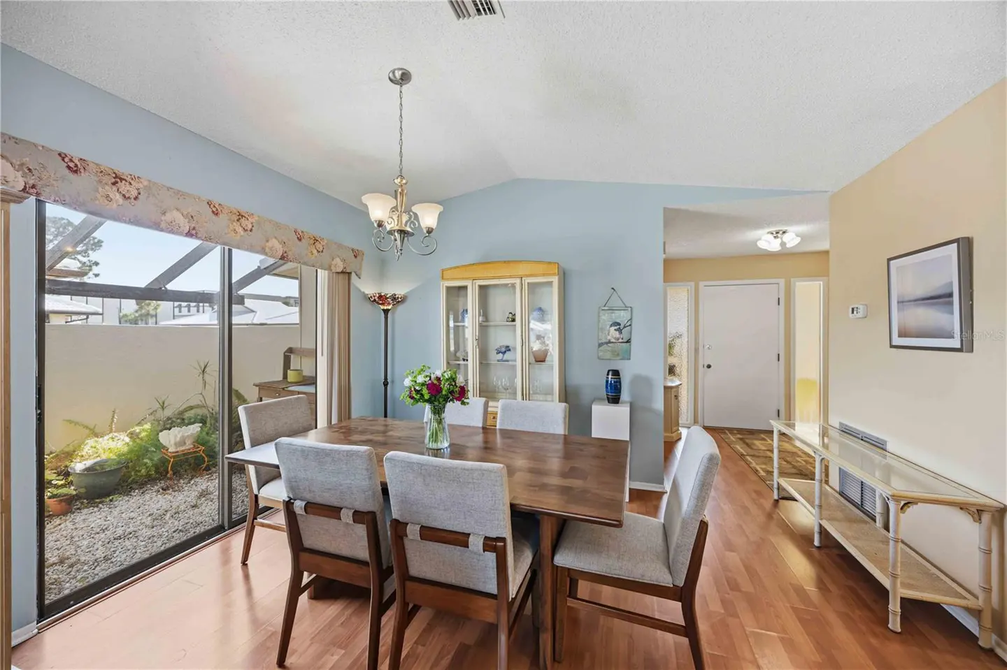 A dining room with a wood table, six chairs, and a glass sliding door to a gravel patio. The walls are blue and beige.