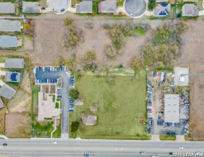 Aerial view of a property with a green field, buildings, parking lots, and a road.
