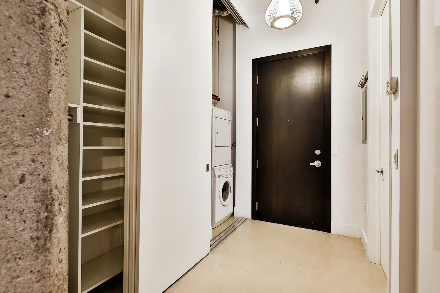 Hallway with built-in shelving, a stacked washer-dryer unit, and a dark brown door under a modern pendant light.