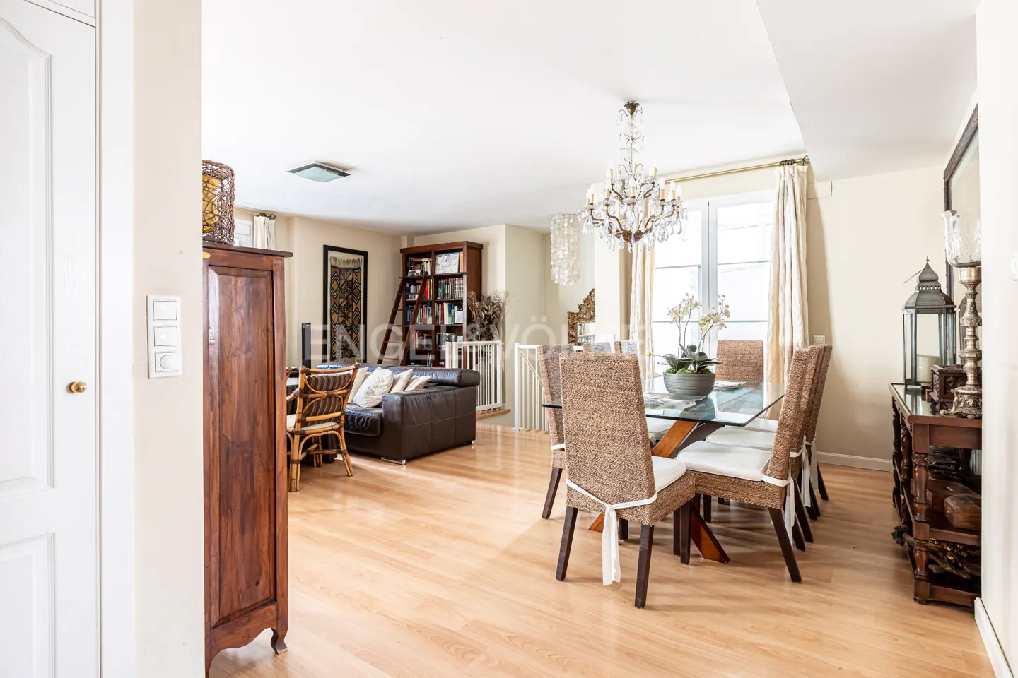 Open-concept living and dining area with hardwood floors, chandelier, and glass-top table with woven chairs. A brown leather sofa is visible.