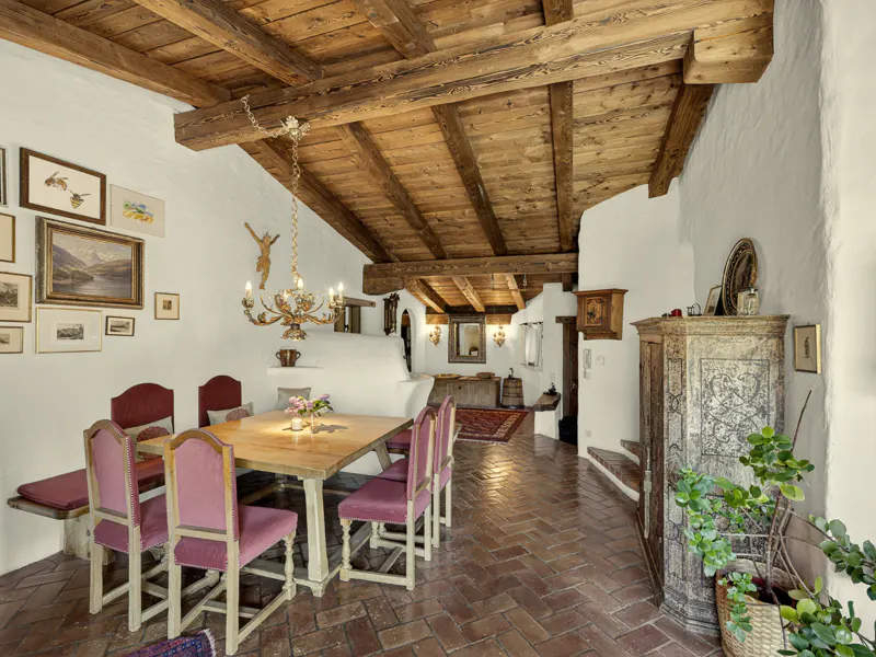 Interior view of a dining room with a wooden ceiling, brick floor, and a large wooden table with pink chairs. A chandelier hangs above the table.