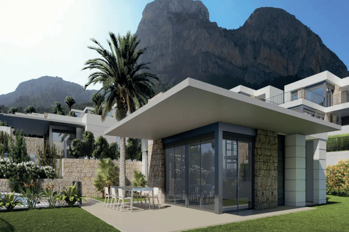 Modern villa with stone accents, glass walls, and a patio with a table and chairs. Palm trees and a mountain backdrop.
