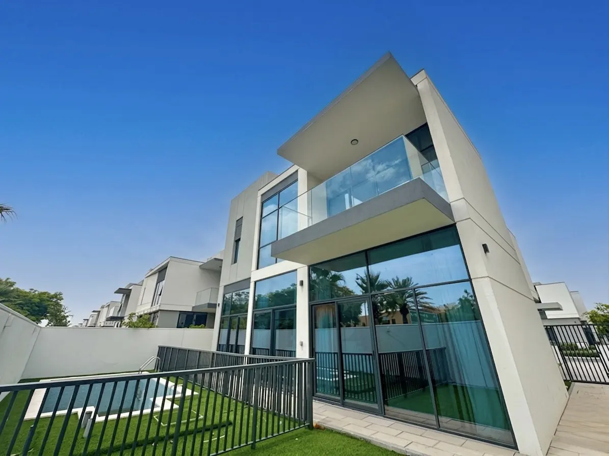 Modern two-story house with a balcony, large windows, and a pool in the backyard under a clear blue sky.