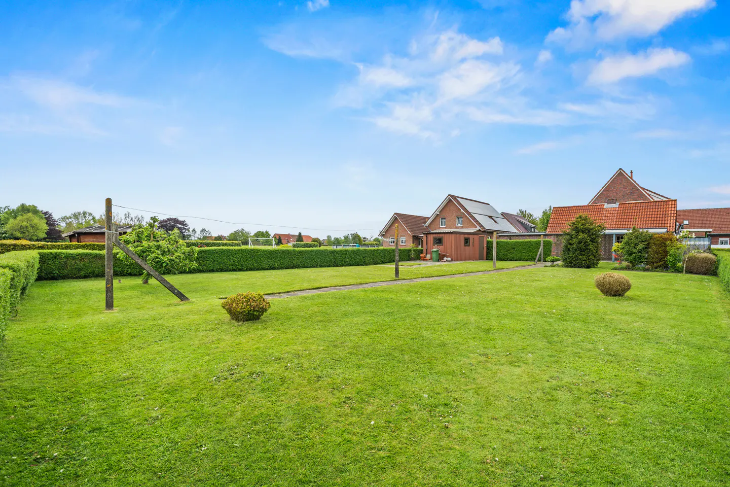 A lush green lawn with trimmed hedges, houses in the background, and a blue sky.