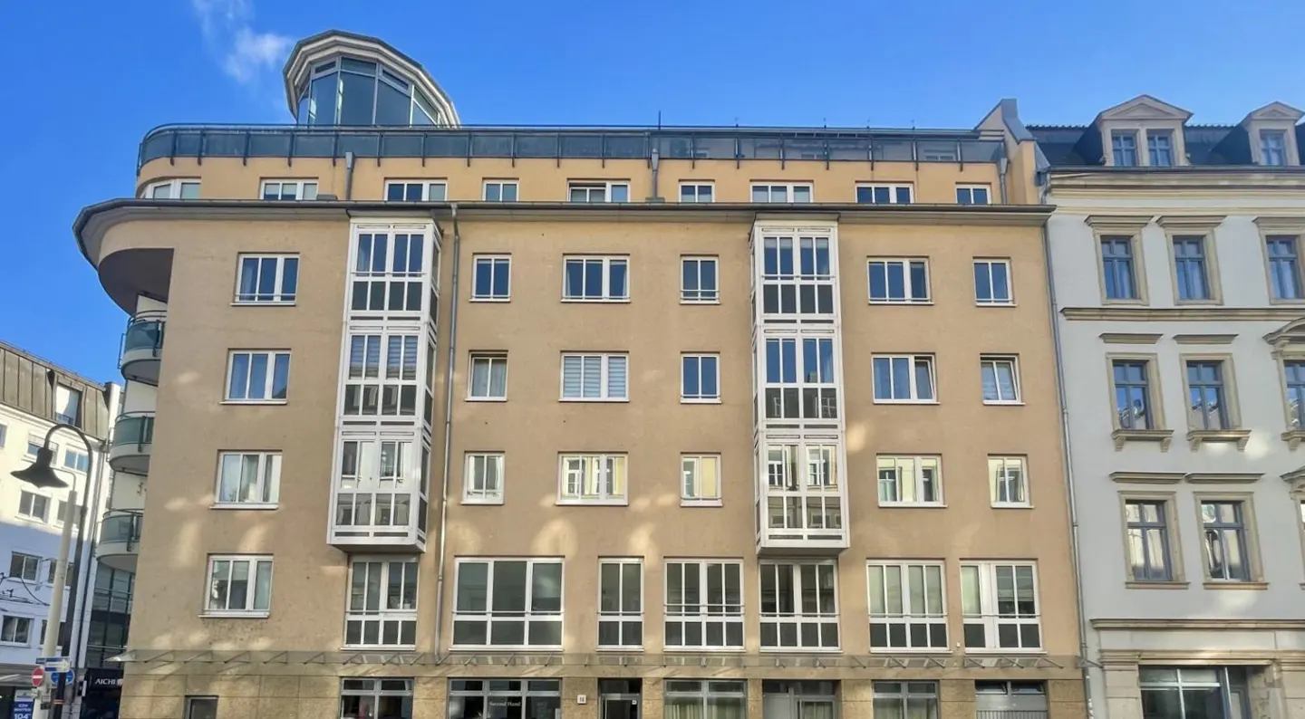 A tan apartment building with white framed windows under a clear blue sky.