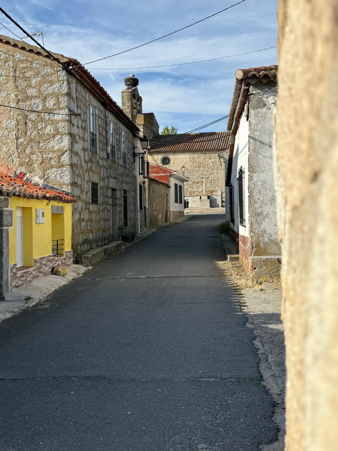 A street view of a European village with stone buildings and a church with a stork nest on top.