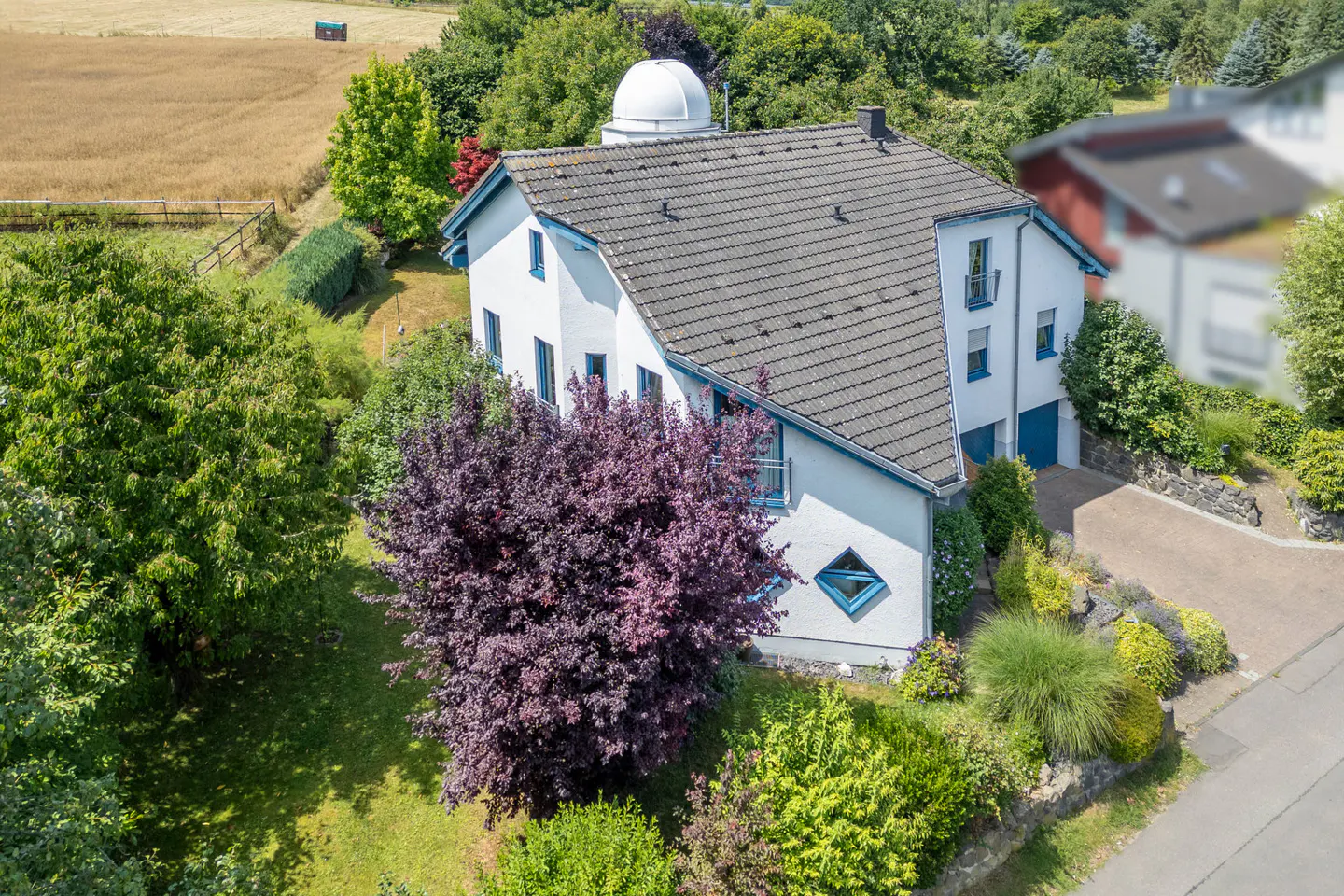Aerial view of a white two-story house with a gray roof and a white dome on top, surrounded by green trees.