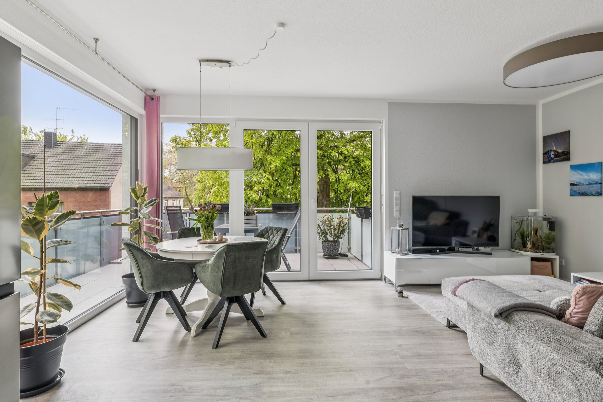 Modern living room with dining area, grey chairs, white table, large windows, balcony access, and a grey sofa.