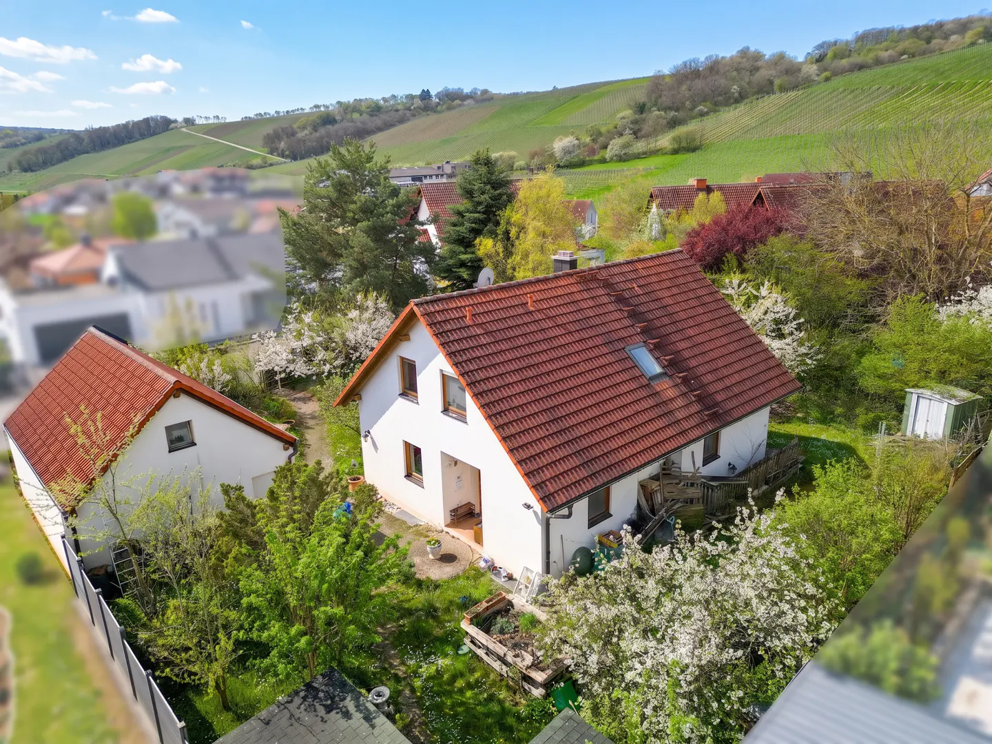 Aerial view of a white house with a red tile roof, surrounded by green trees and a hillside in the background.