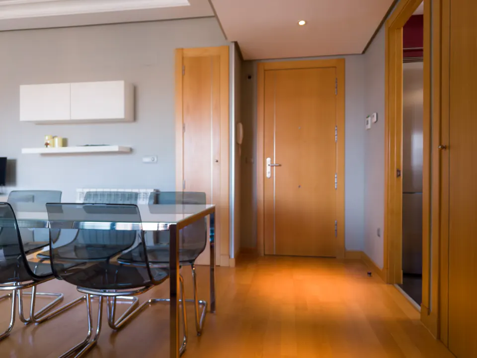 Interior view of a modern apartment with a glass table, chairs, wood floors, and doors.