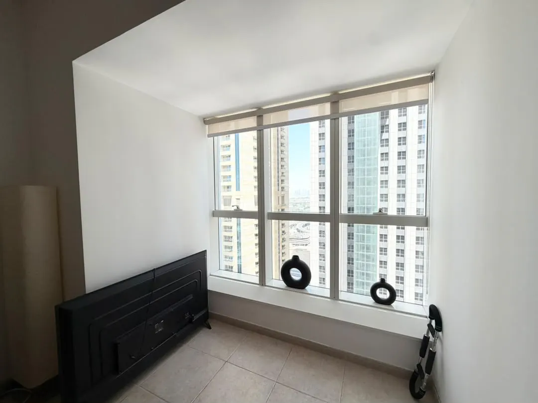 A room with a large window overlooking city skyscrapers, featuring two black circular vases on the sill and a flat-screen TV.