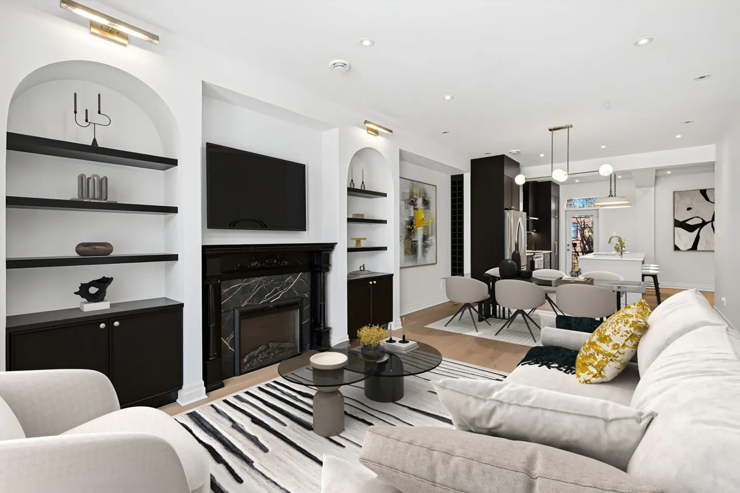 Bright, modern living room with black fireplace, TV, and built-in shelves. A white sofa and round glass coffee table sit on a striped rug.