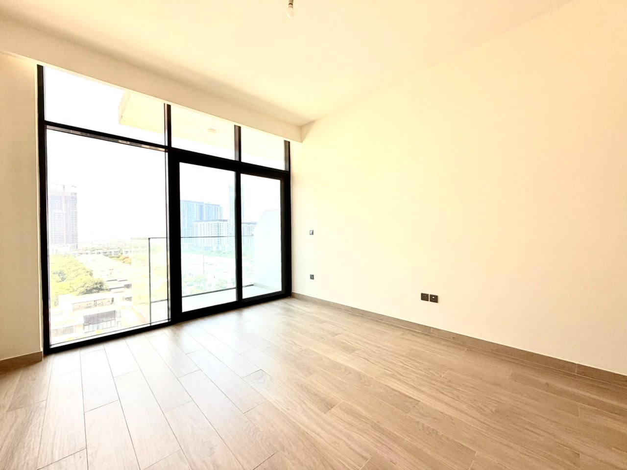 Empty room with light wood-look tile floors, cream walls, and floor-to-ceiling windows overlooking a city skyline.