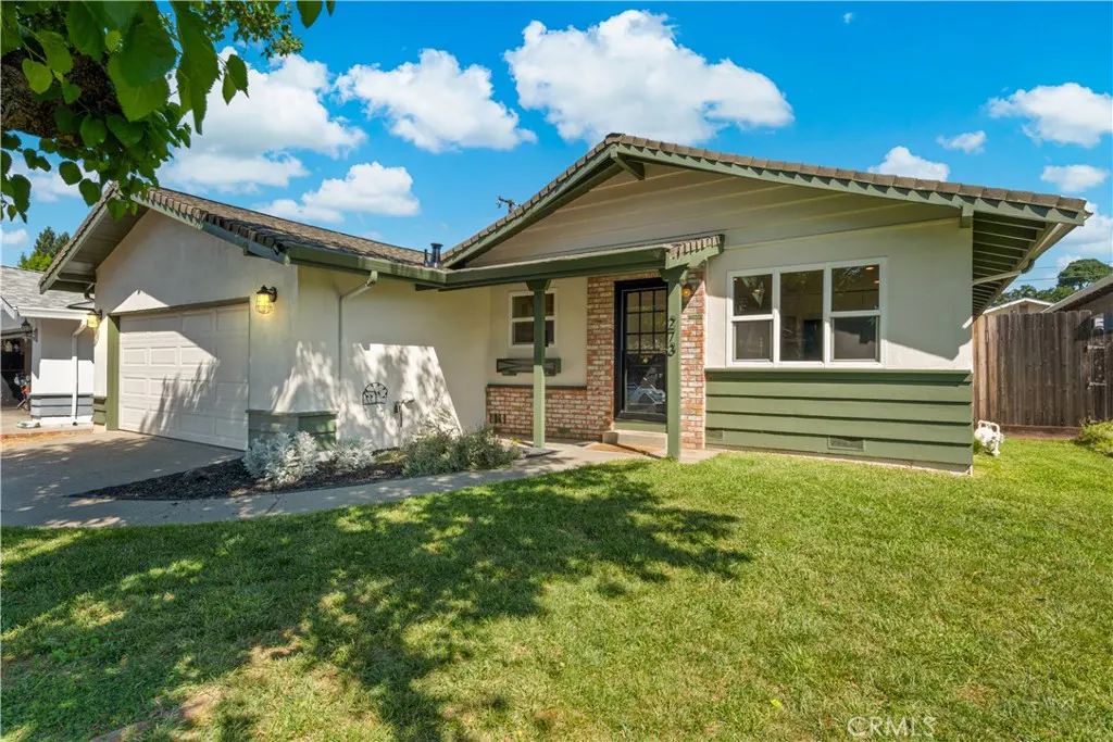 A single-story home with a white exterior, green trim, and a brown roof under a blue sky with clouds. A green lawn is in front.