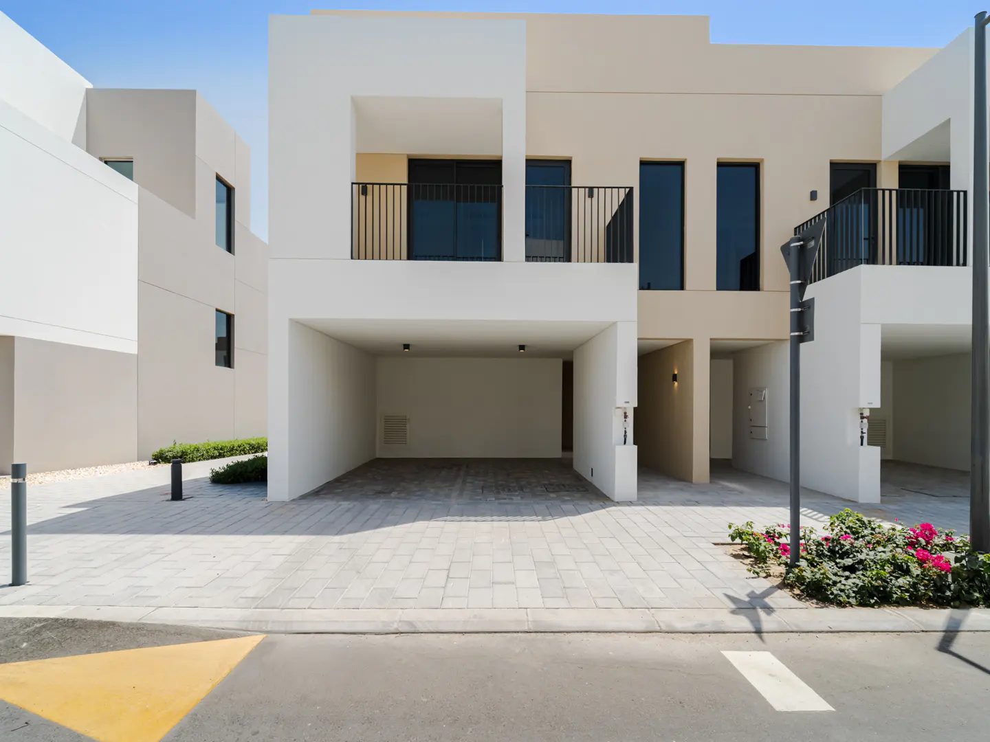 Modern townhouses with open carports, black railings, and neutral color schemes under a clear blue sky.