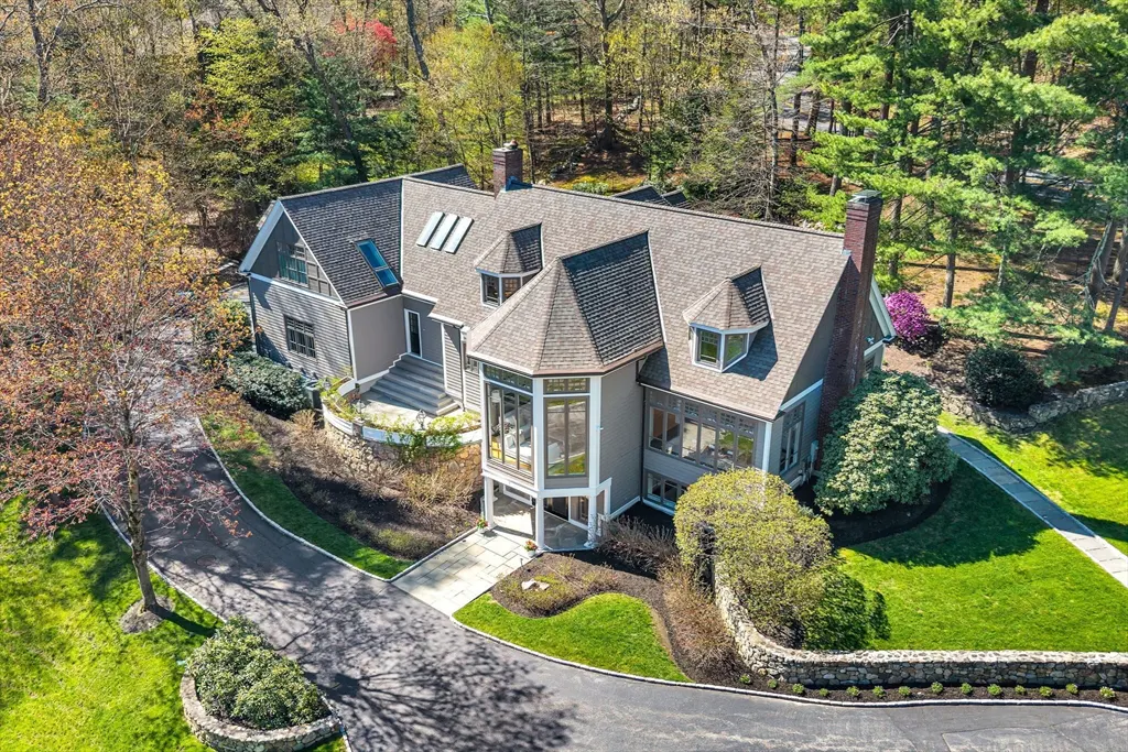 Aerial view of a gray two-story house with a dark roof, surrounded by green trees and a winding driveway.