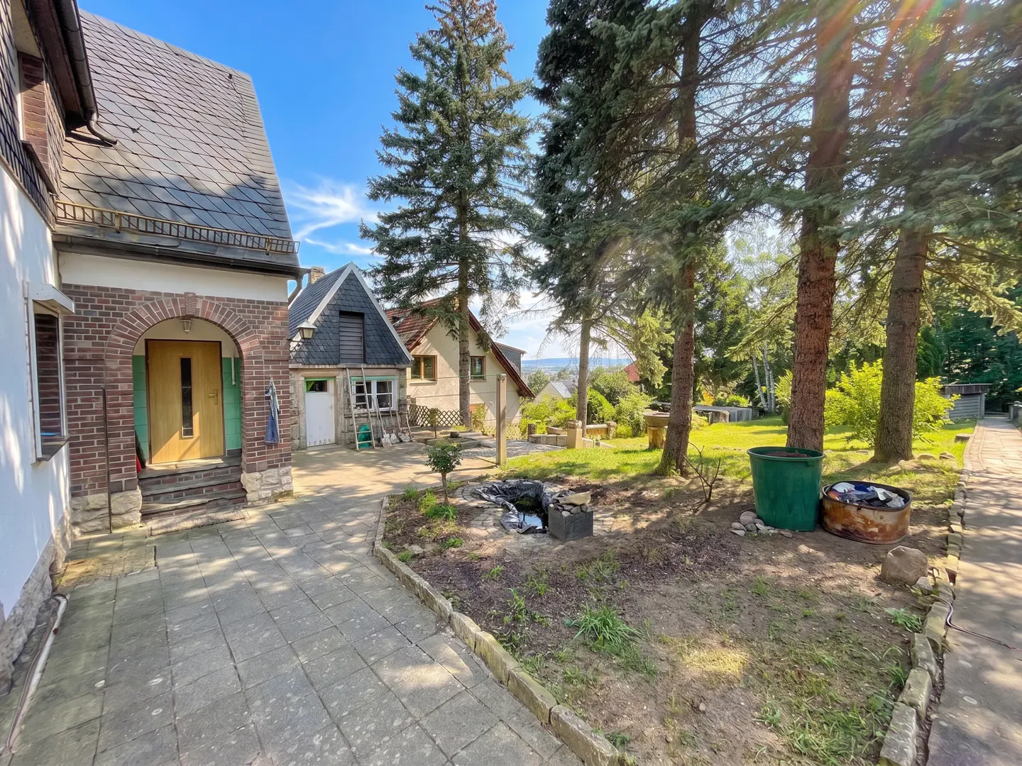Exterior view of a house with a brick archway entrance, a stone path, and a yard with tall trees.