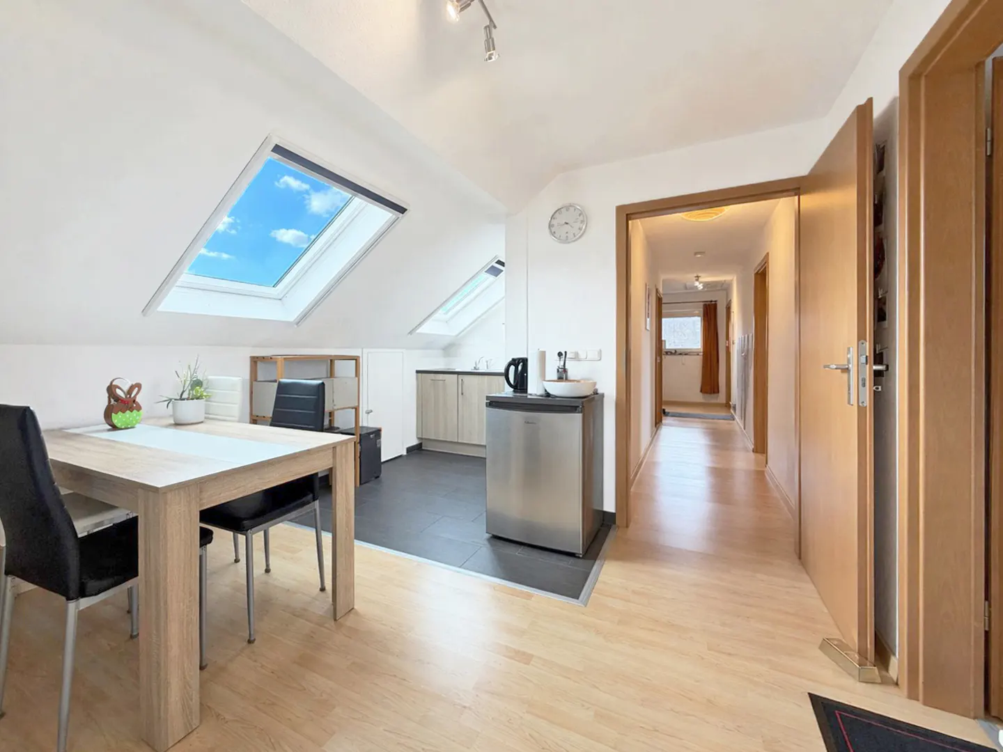 Attic apartment interior with skylights, dining table, kitchenette, and hallway with wood floors and doors.