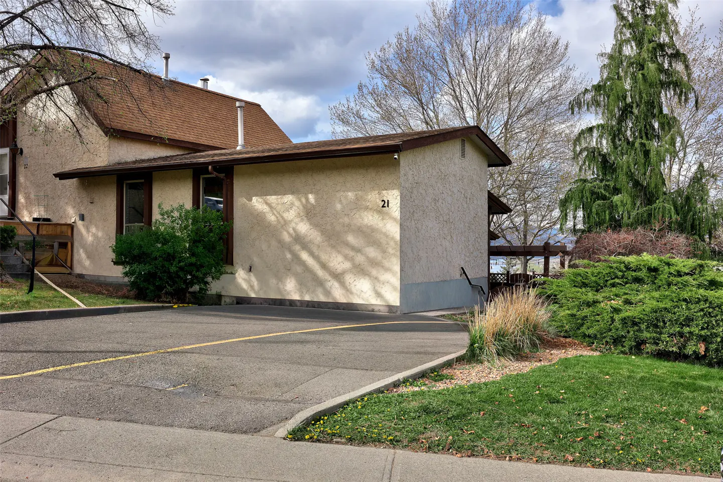 Exterior view of a beige stucco house with a brown roof and the number 21 on the side, with a paved driveway and green lawn.