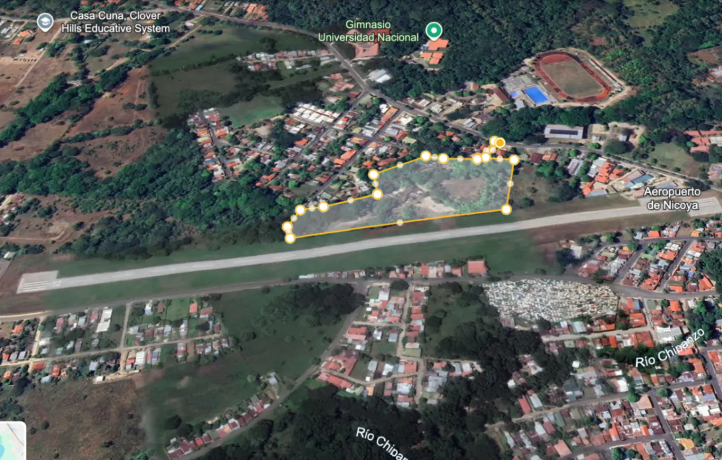 Aerial view of a property outlined in yellow, near Nicoya Airport, with houses and trees surrounding it.
