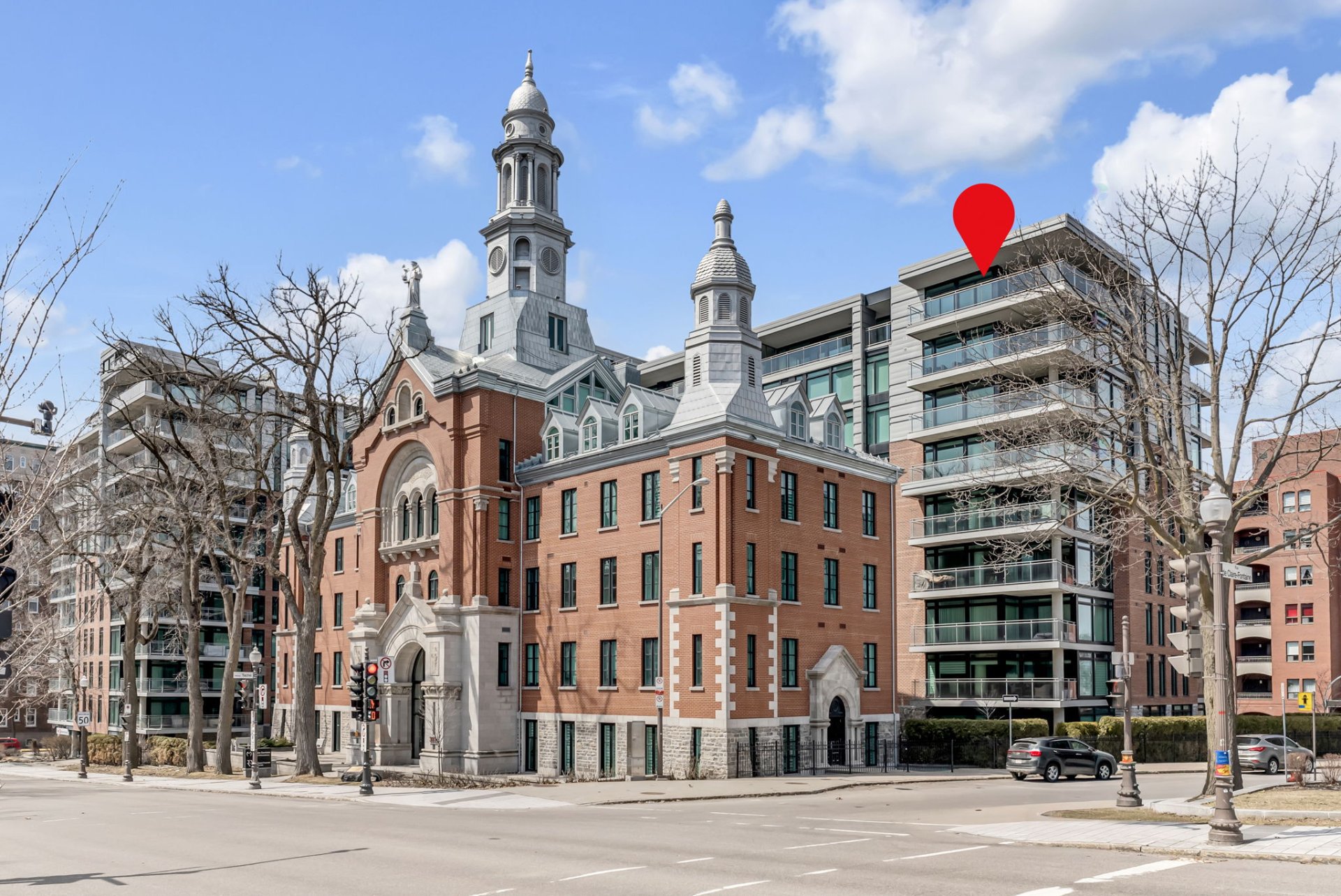 Exterior view of a brick building with a tower and a modern apartment building with a red pin on top.