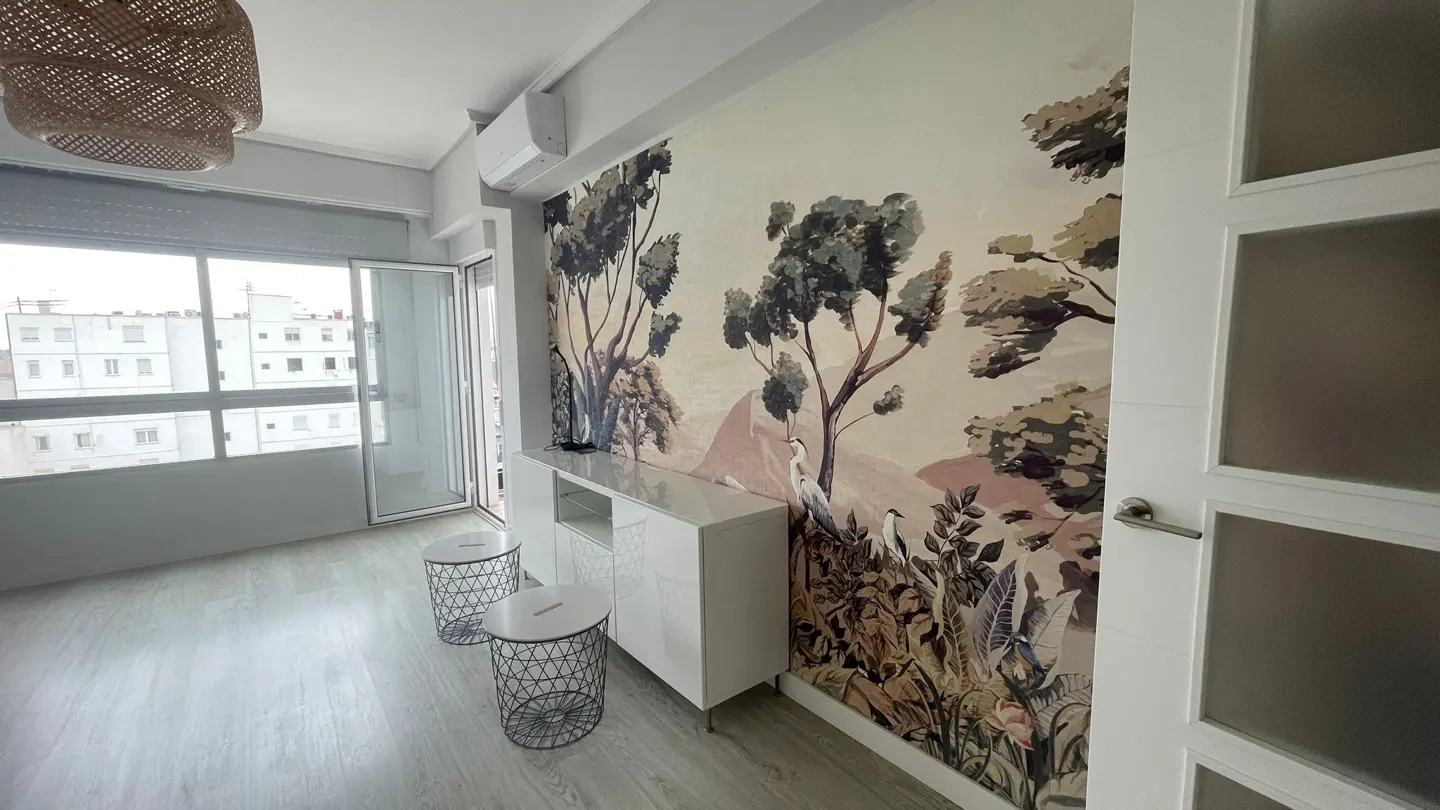Bright room with light wood floors, a white sideboard, two wire stools, and a wall mural featuring trees and birds.