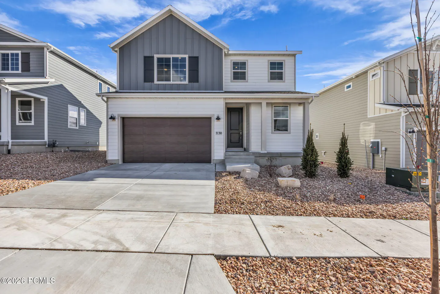 Two-story home with gray and white siding, a brown garage door, and a concrete driveway under a blue sky.