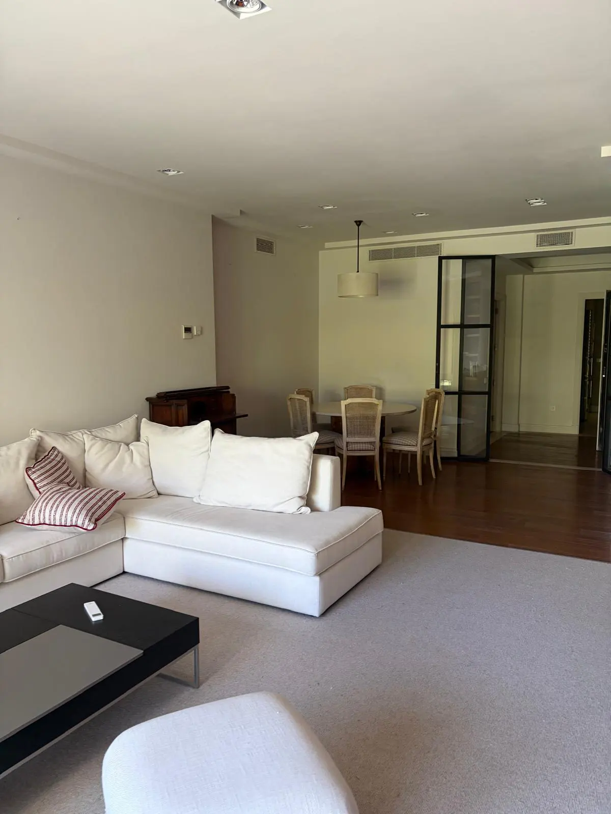 A bright, open-concept living and dining area with a white sectional sofa, black coffee table, and dining set.