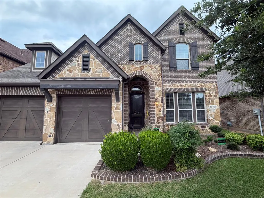 Two-story brick and stone house with a two-car garage and manicured lawn on a cloudy day.