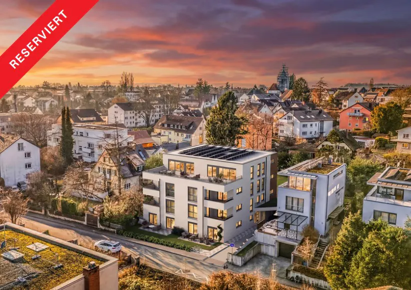 Reserved modern white apartment building with solar panels, surrounded by a European town at sunset.
