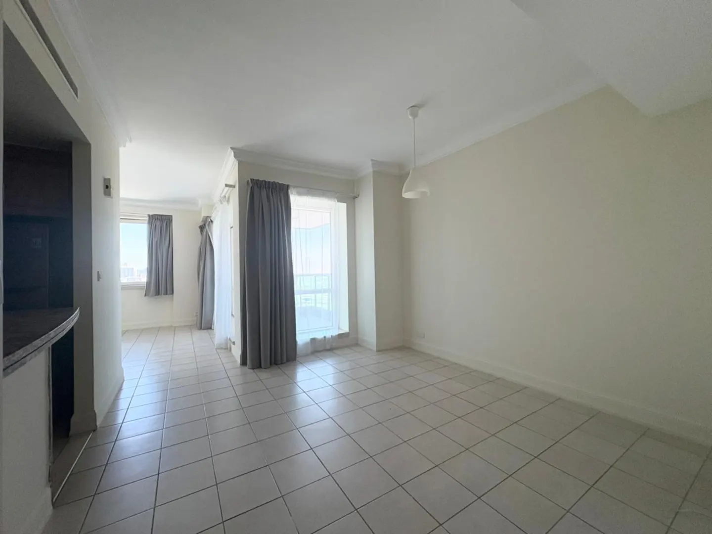 A bright, empty room with tile flooring and large windows with gray curtains.