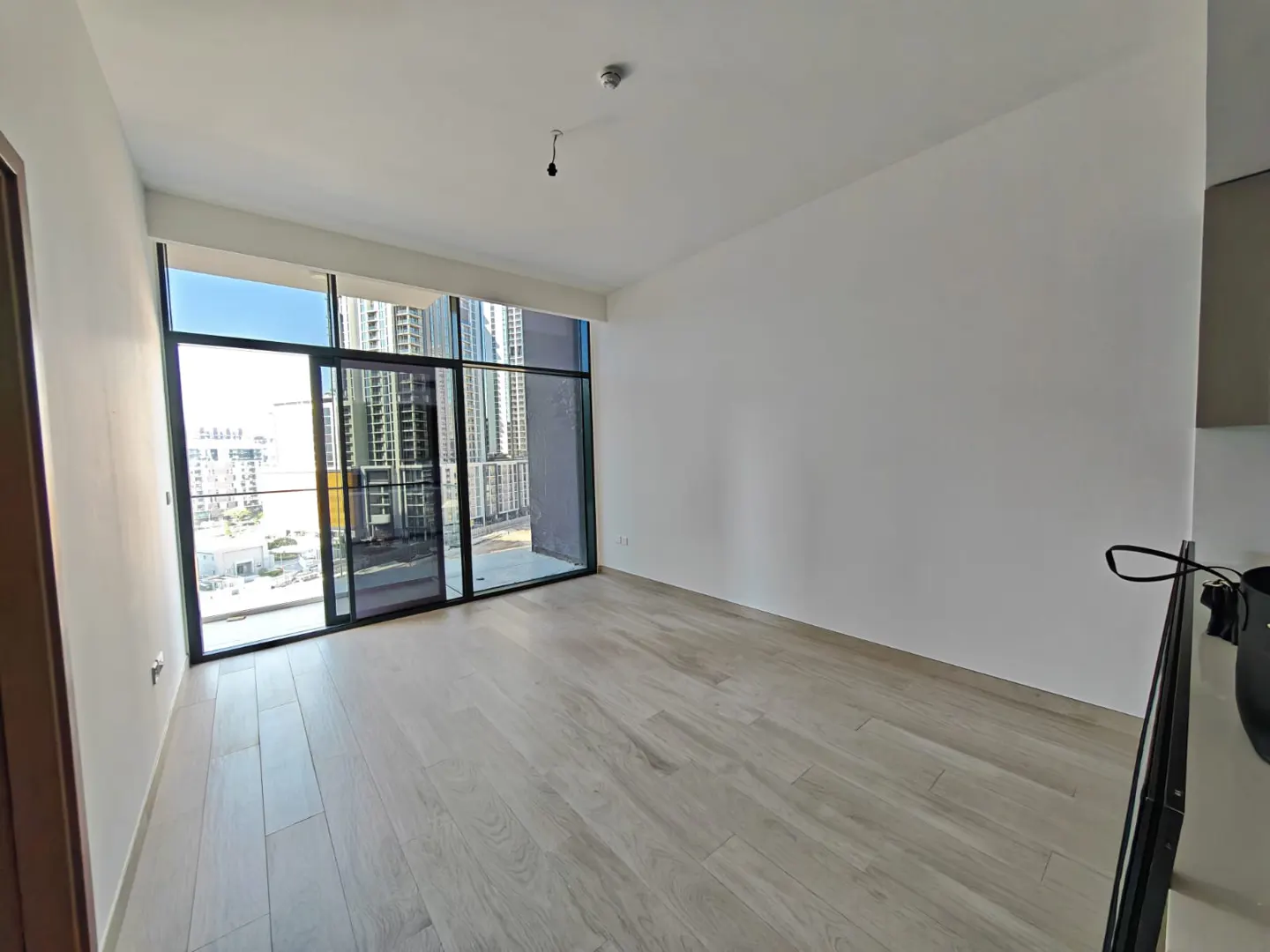 Empty room with light wood floors, white walls, and a large window with a city view.