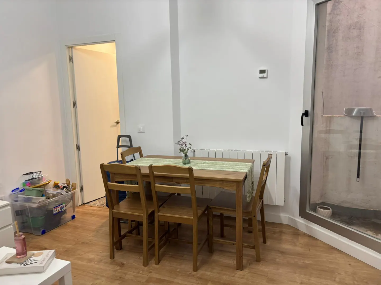 A wooden dining table with four chairs and a green runner sits in a room with white walls and light wood flooring.