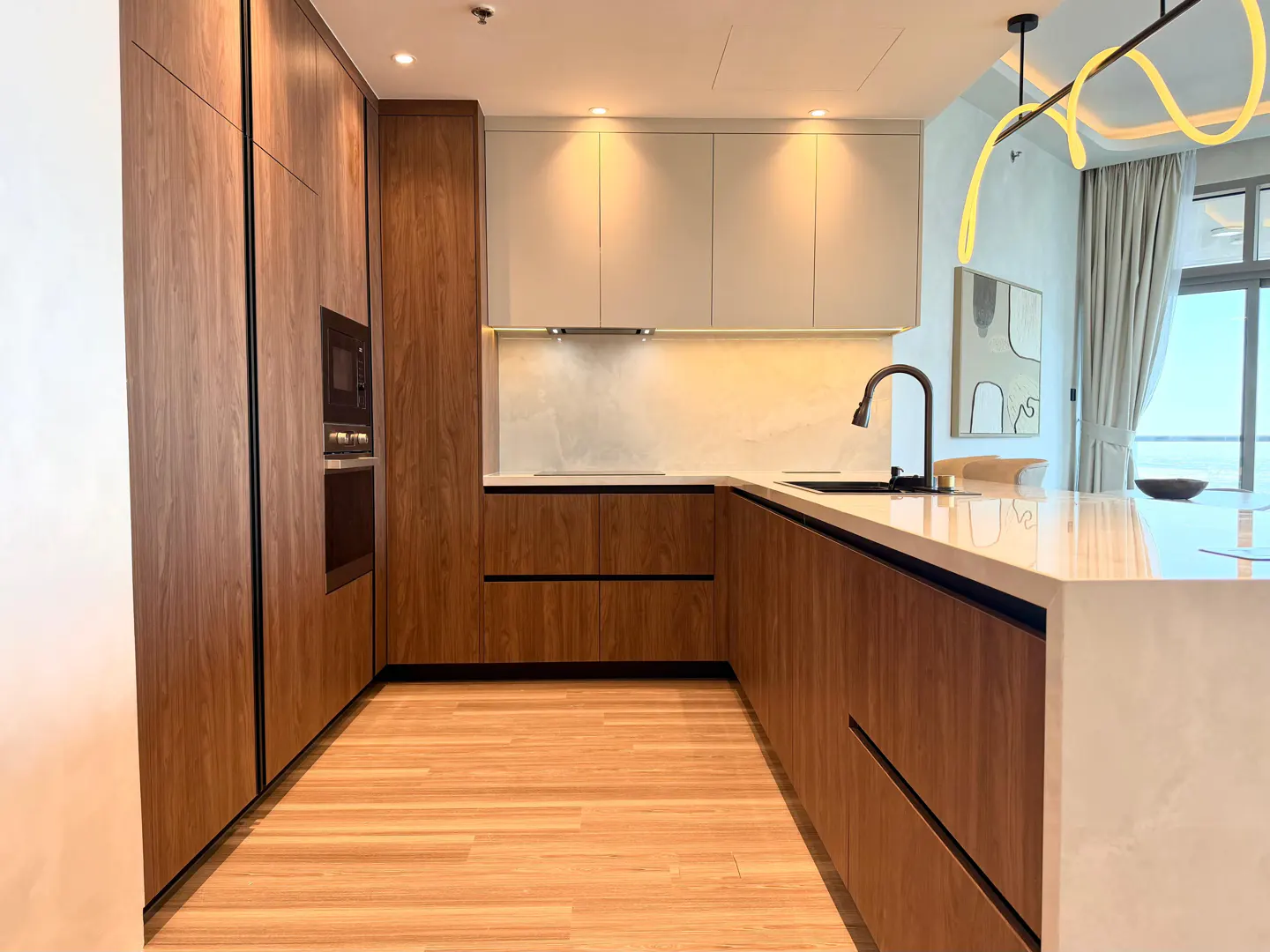 A modern kitchen with wood cabinets, a white countertop, and a black faucet. A window with curtains is in the background.