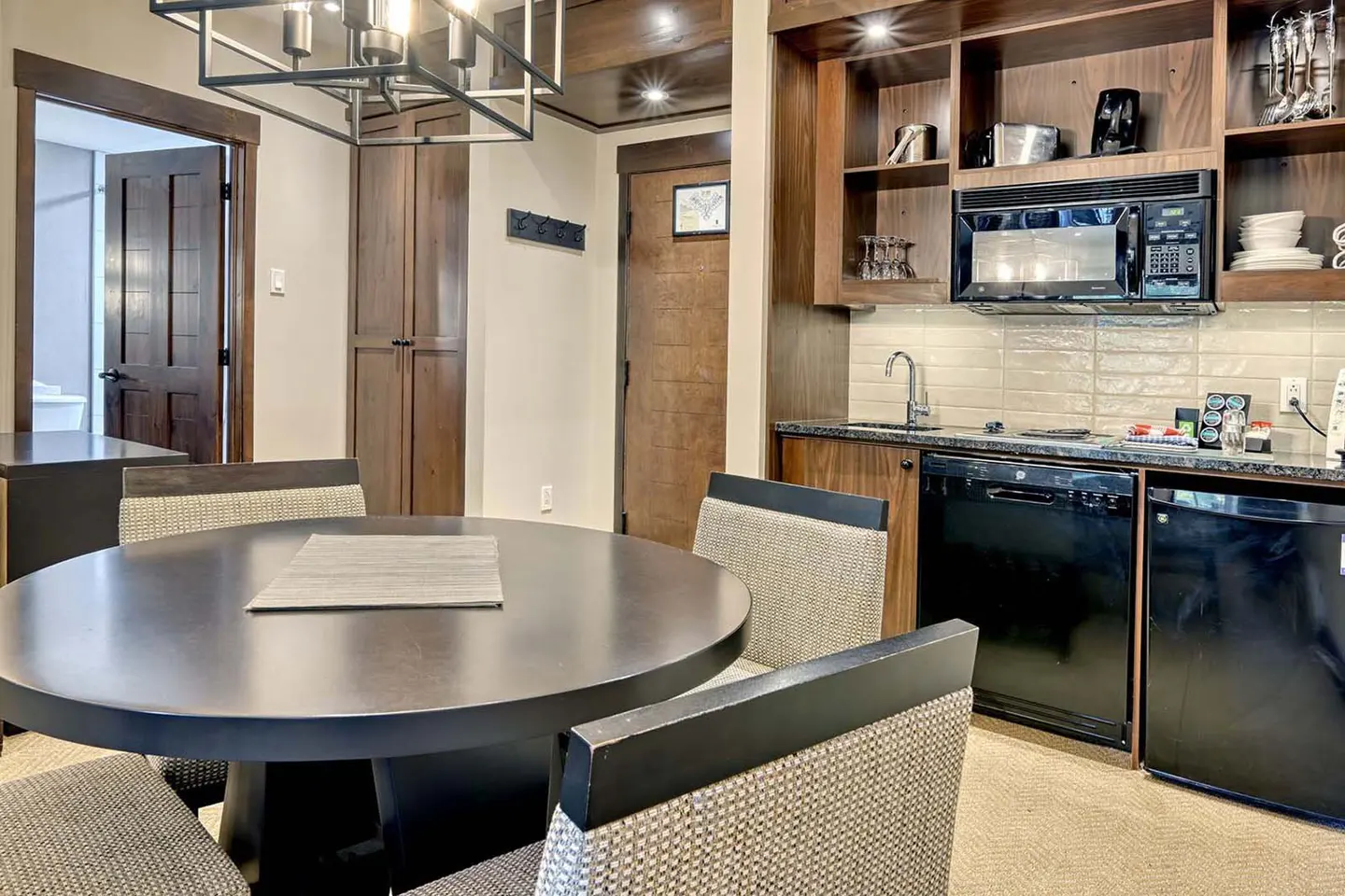 Interior view of a dining area with a dark wood table and chairs, a kitchenette with black appliances, and wood cabinets.