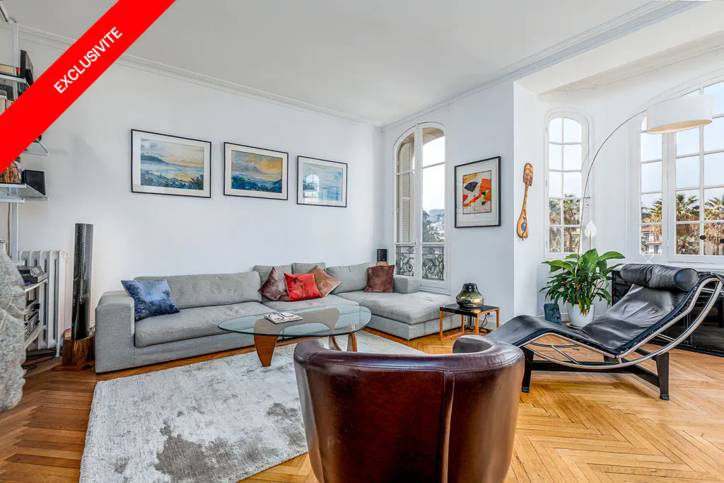 Bright living room with hardwood floors, a gray sectional sofa, a glass coffee table, and a black chaise lounge near large windows.