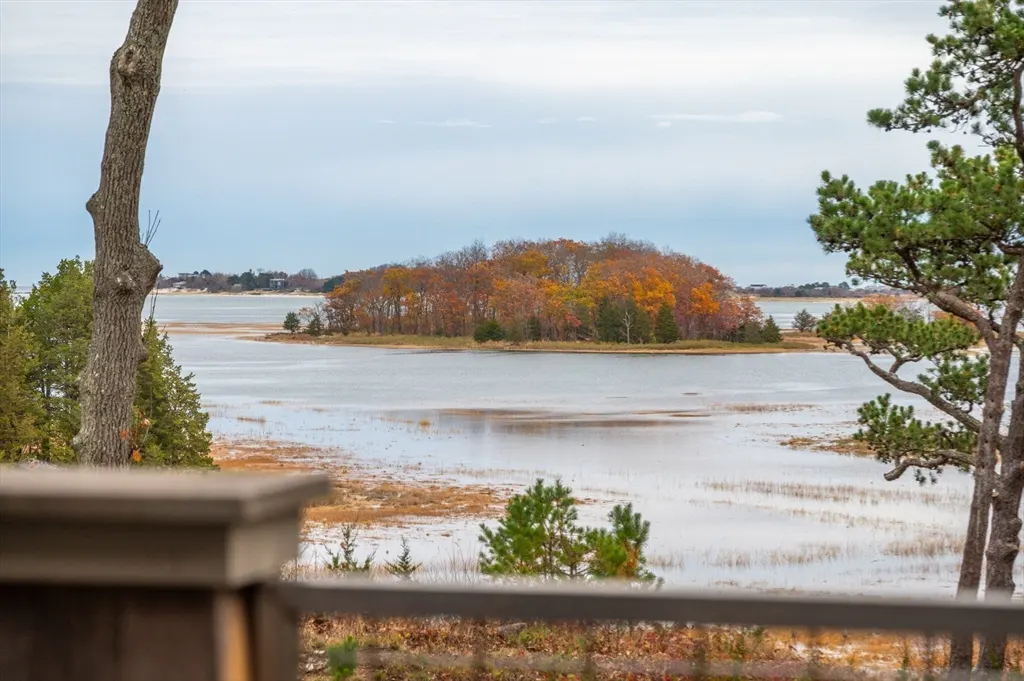 Water view of an island with fall foliage, seen from a deck with trees on either side.