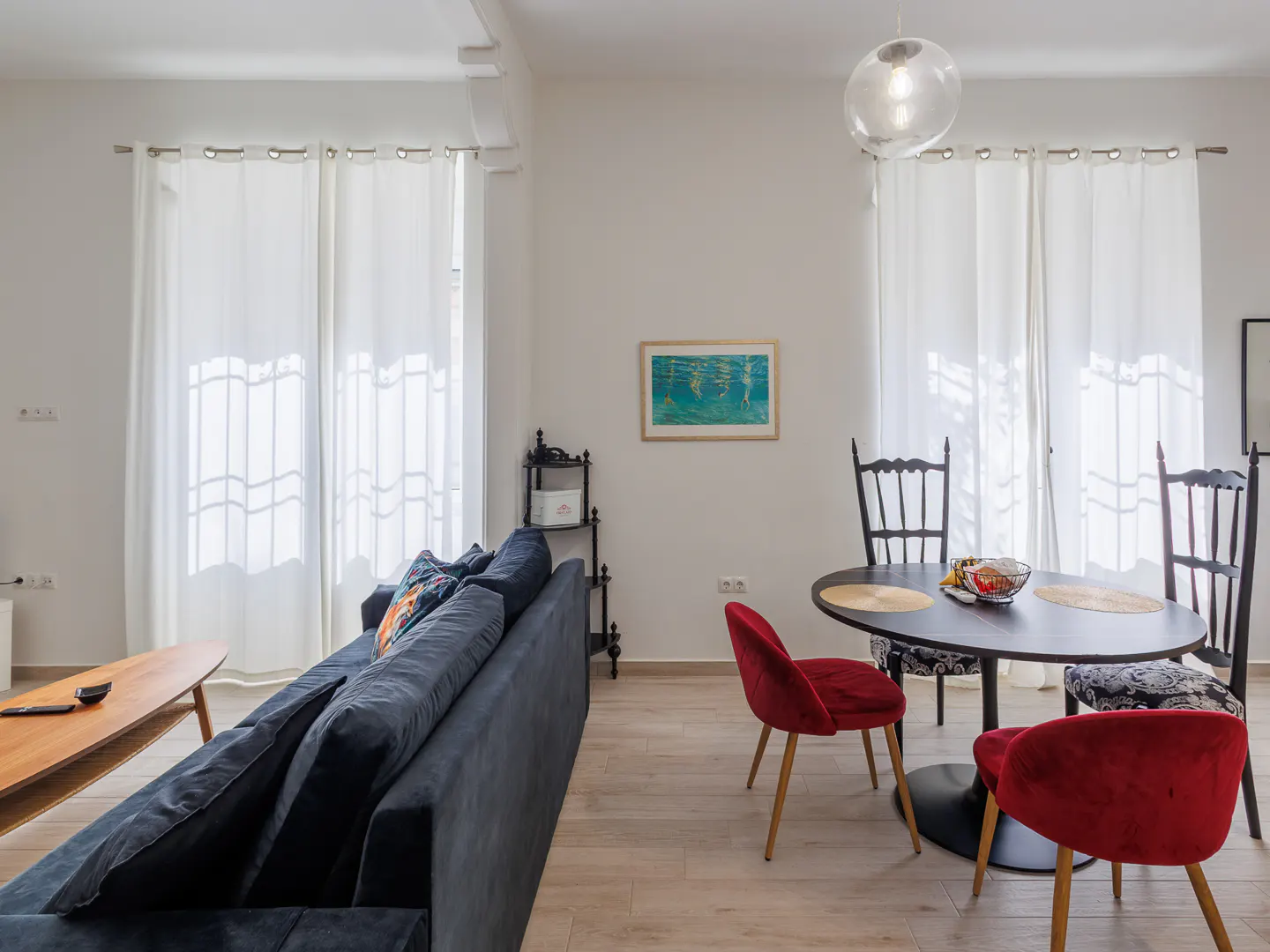 Living room with a blue sofa, a black table with red chairs, and white curtains.