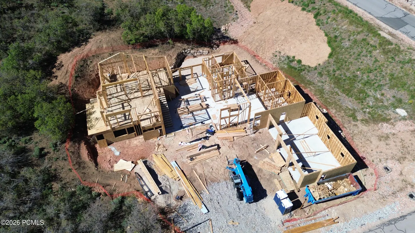 Aerial view of a wooden house frame under construction on a sloped, wooded lot with a blue dumpster and construction gear.