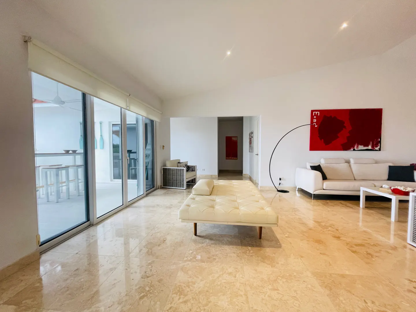 Bright living room with marble floors, white walls, and a large sliding glass door to a patio. A white couch and daybed furnish the space.