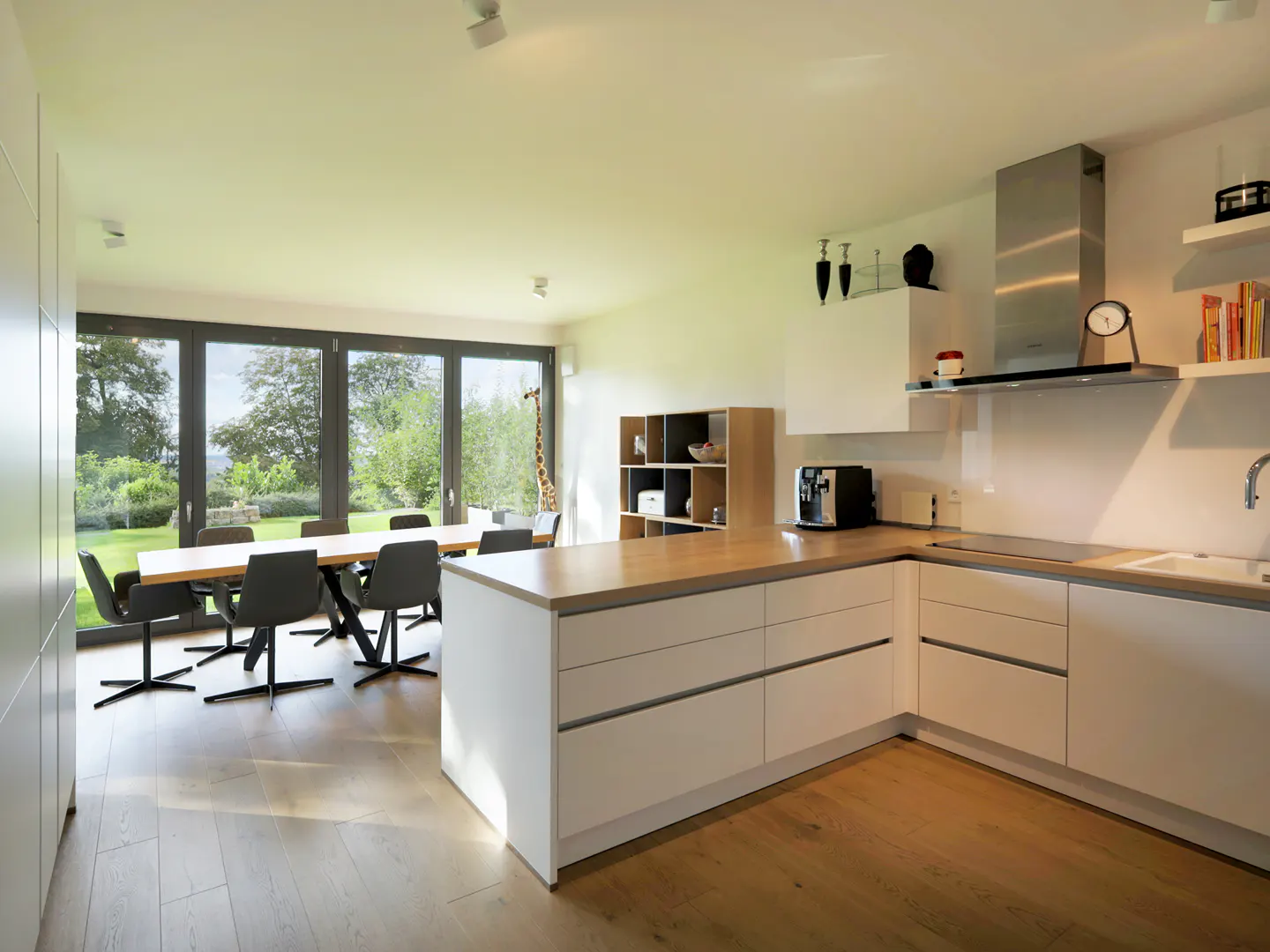 Bright, modern kitchen with white cabinets, wood countertops, and stainless steel appliances. Dining table and chairs visible through large windows.