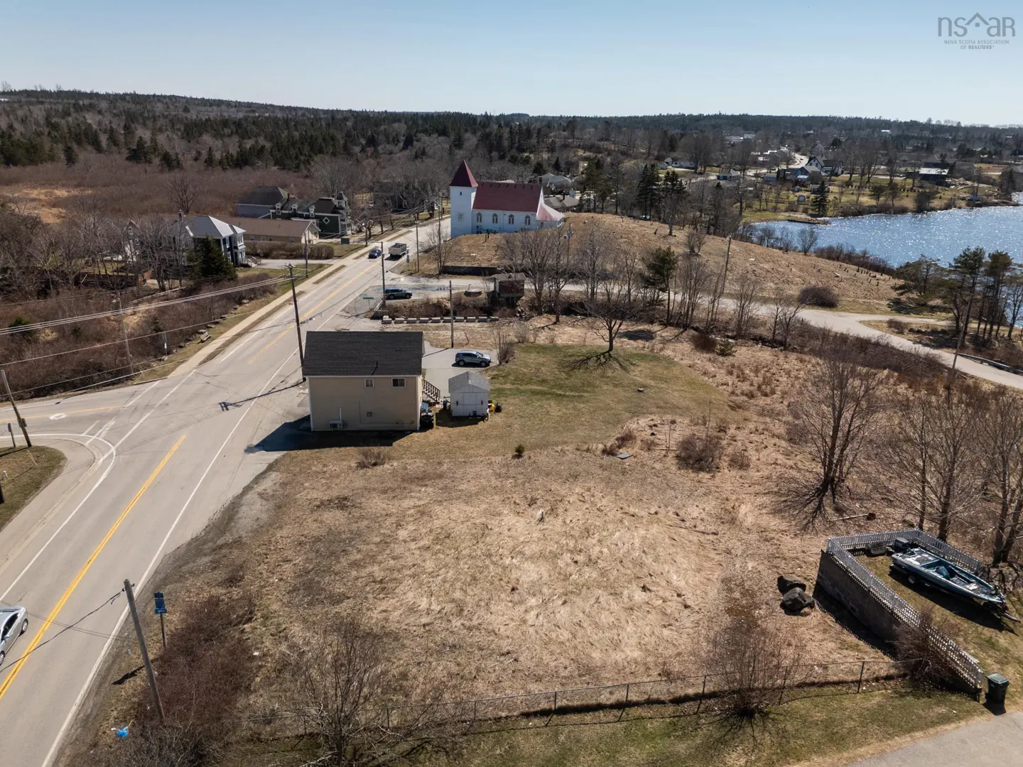 Aerial view of a vacant lot with a tan house, a church with a red roof, and a glimpse of a blue lake in the background.