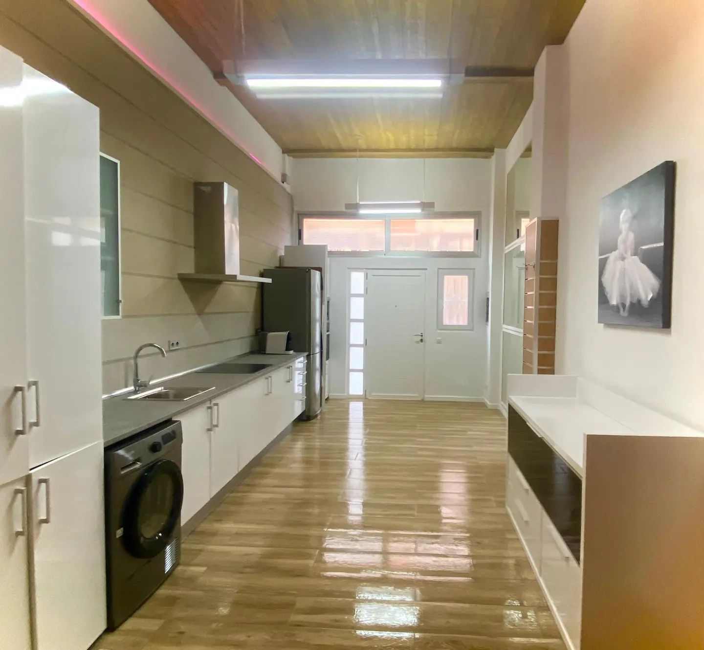 Modern kitchen with white cabinets, stainless steel appliances, wood-look flooring, and a ballerina print on the wall.