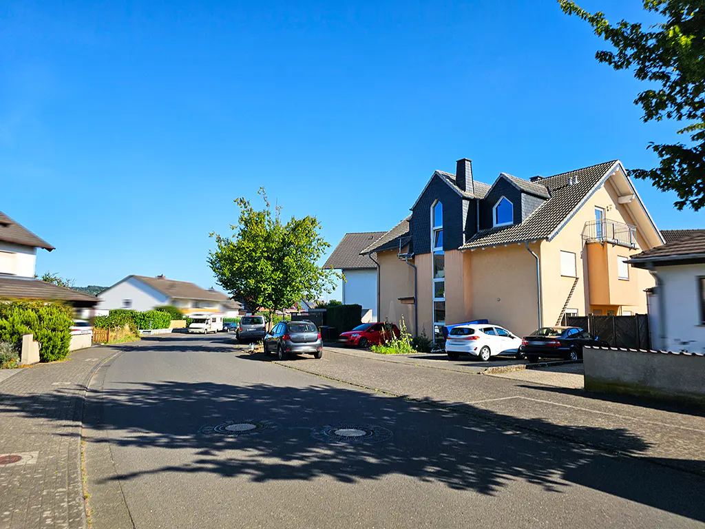 Street view of a residential area with parked cars and houses under a clear blue sky.