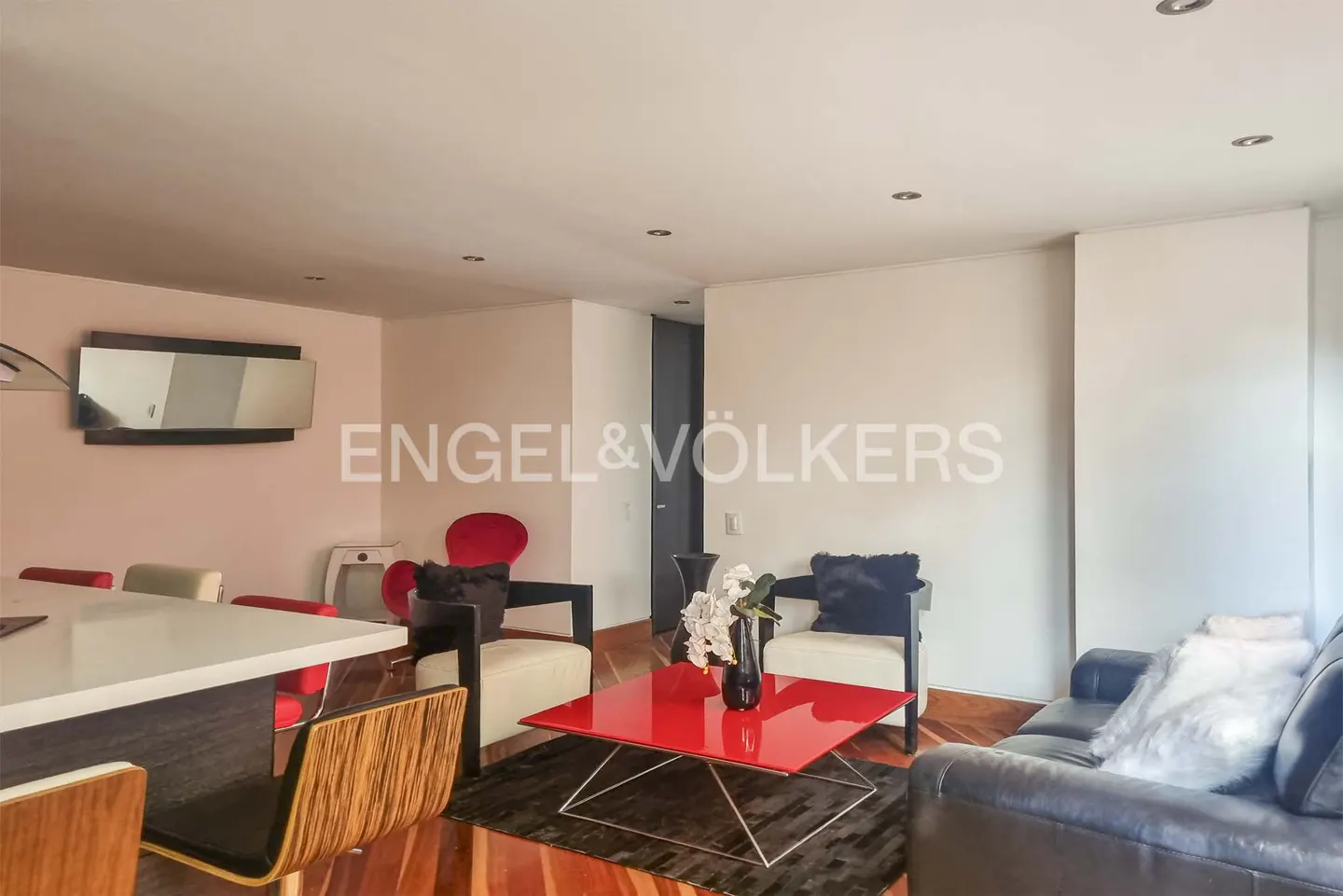 A modern living room with a red coffee table, black rug, and leather sofa. Engel & Völkers logo is visible.